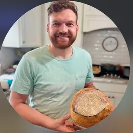 The baker in his kitchen, holding a round loaf